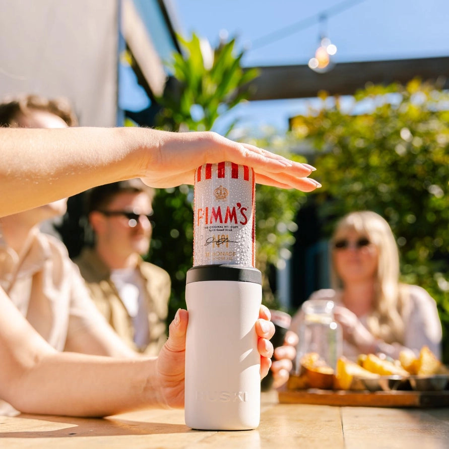 Person holding a Pimm's can with a white tumbler outdoors.