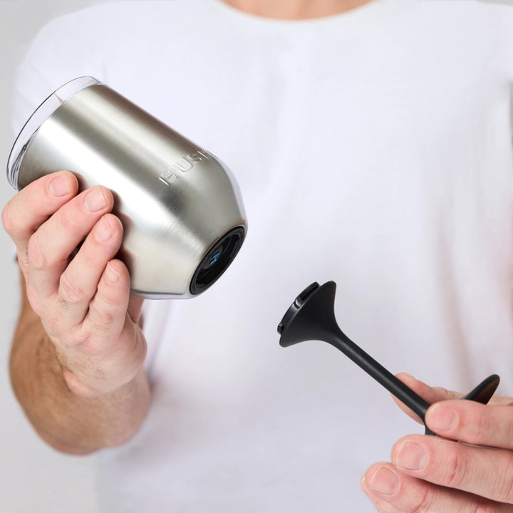 Person holding a silver cup with a black lid and straw on a white background