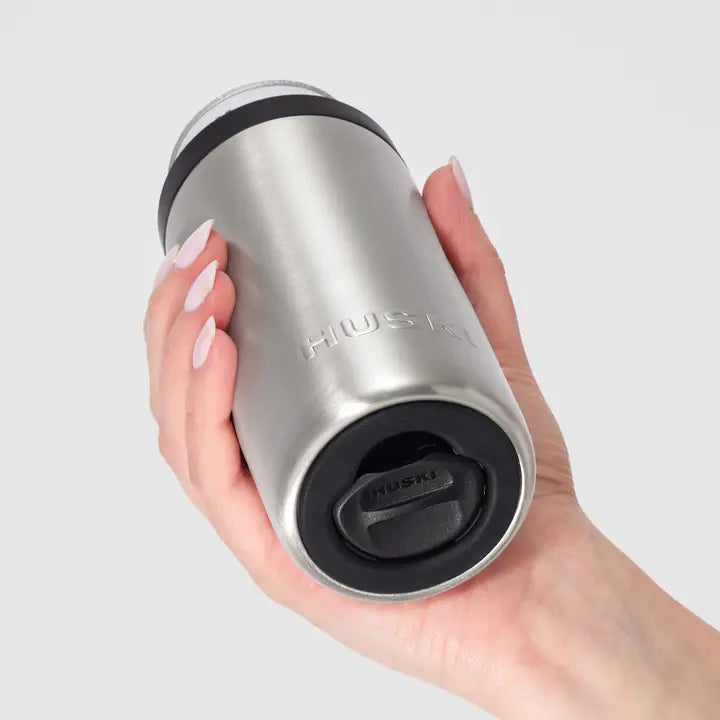 Hand holding a silver insulated tumbler with black lid on a light gray background