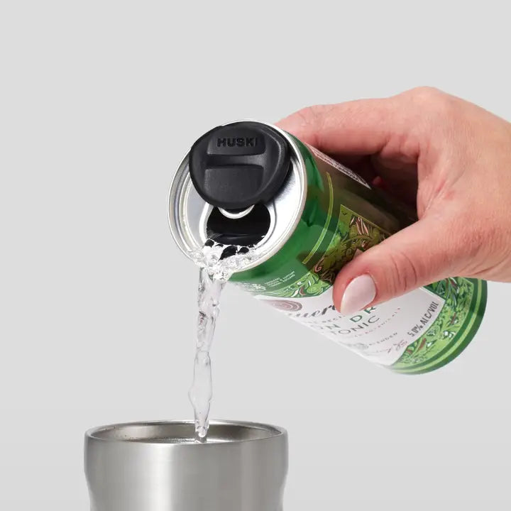Hand pouring liquid from a green bottle into a silver cup on a light gray background