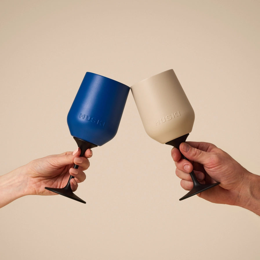 Two hands holding blue and beige wine glasses against a beige background