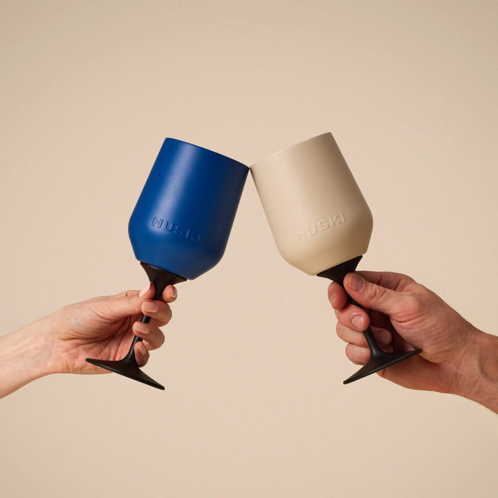 Two hands holding blue and beige wine glasses against a beige background
