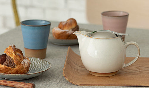 Teapot on a wooden tray with pastries and cups in the background