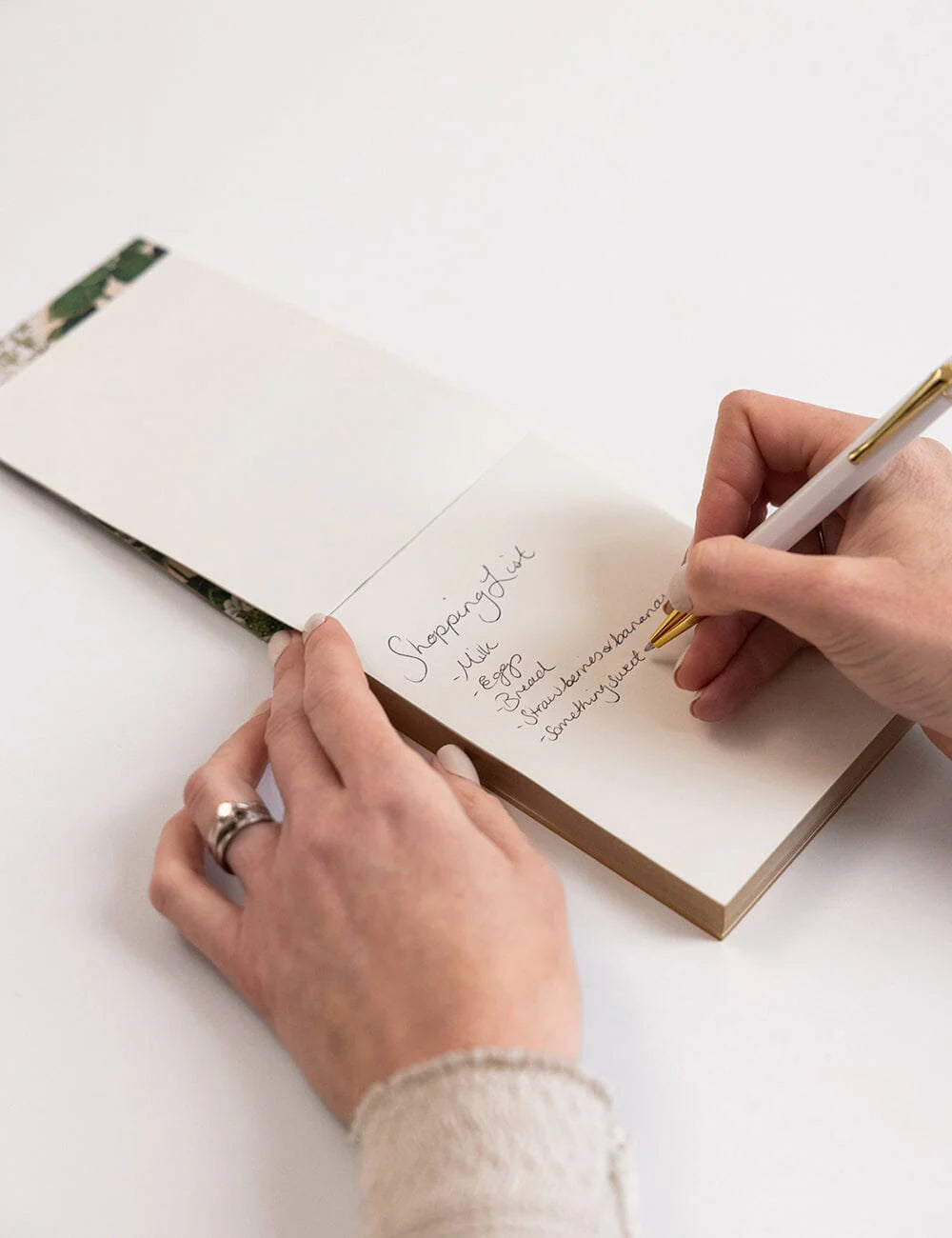 Person writing in a notebook with a pen on a white surface