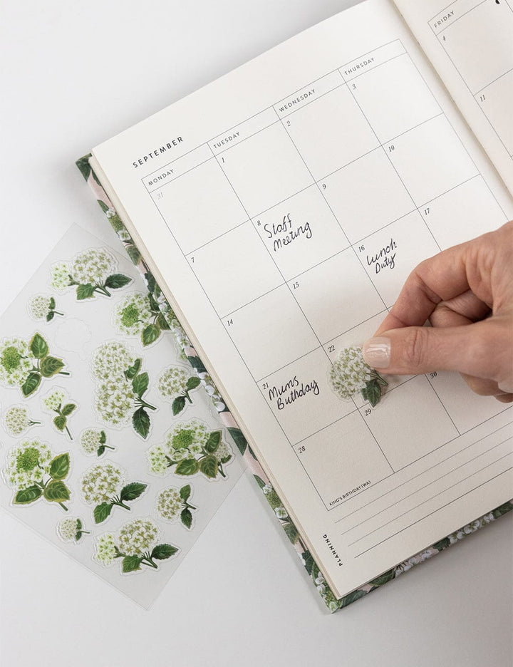 Hand placing a floral sticker on a planner page with a floral cover.