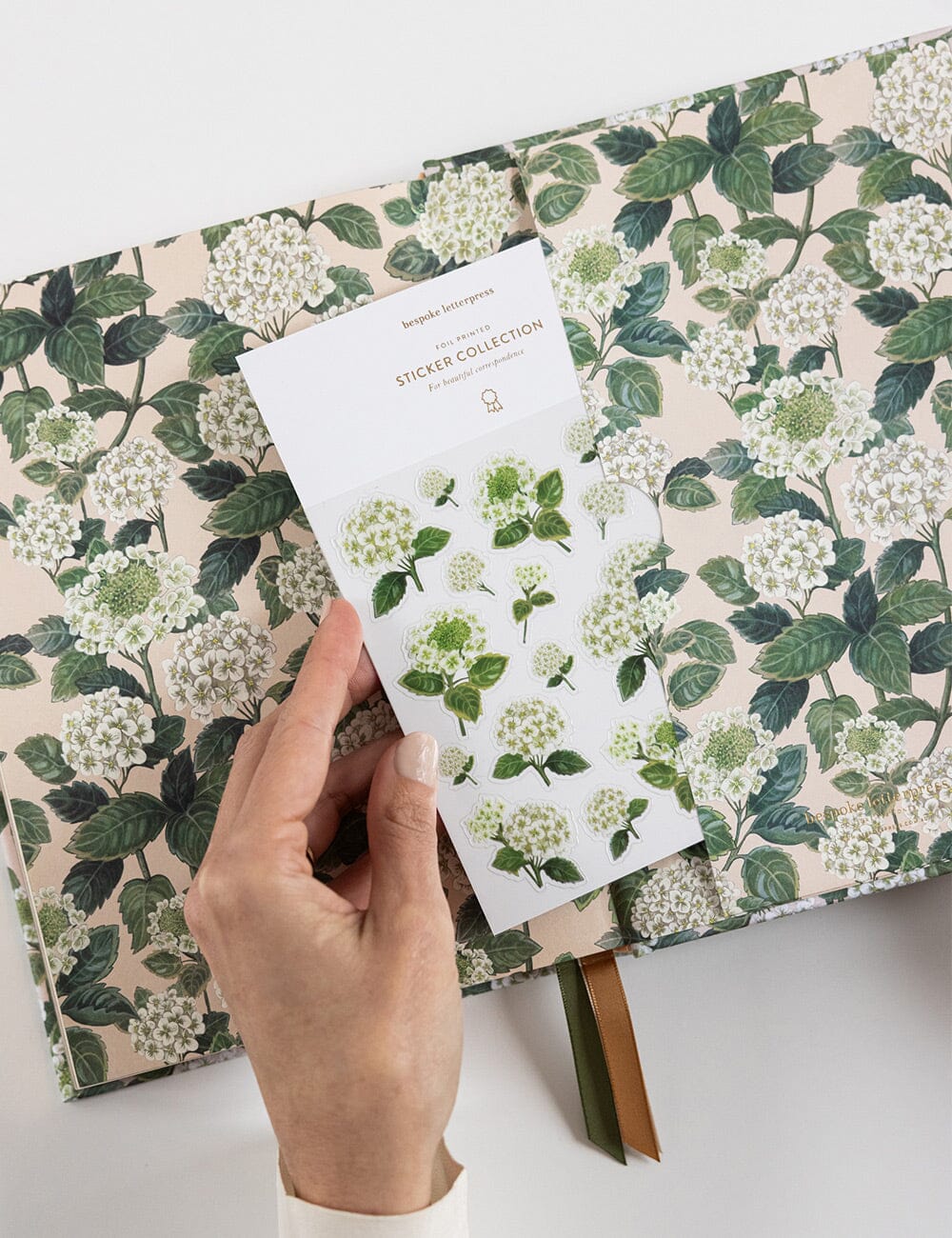 Hand holding a sheet of floral stickers over a notebook with a floral design.