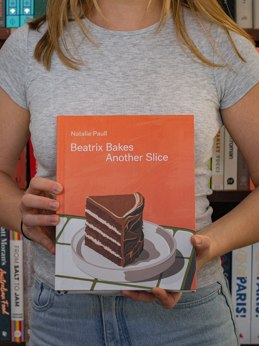 A person holding a book titled 'Beatrix Bakes Another Slice' by Nastasia Paul.