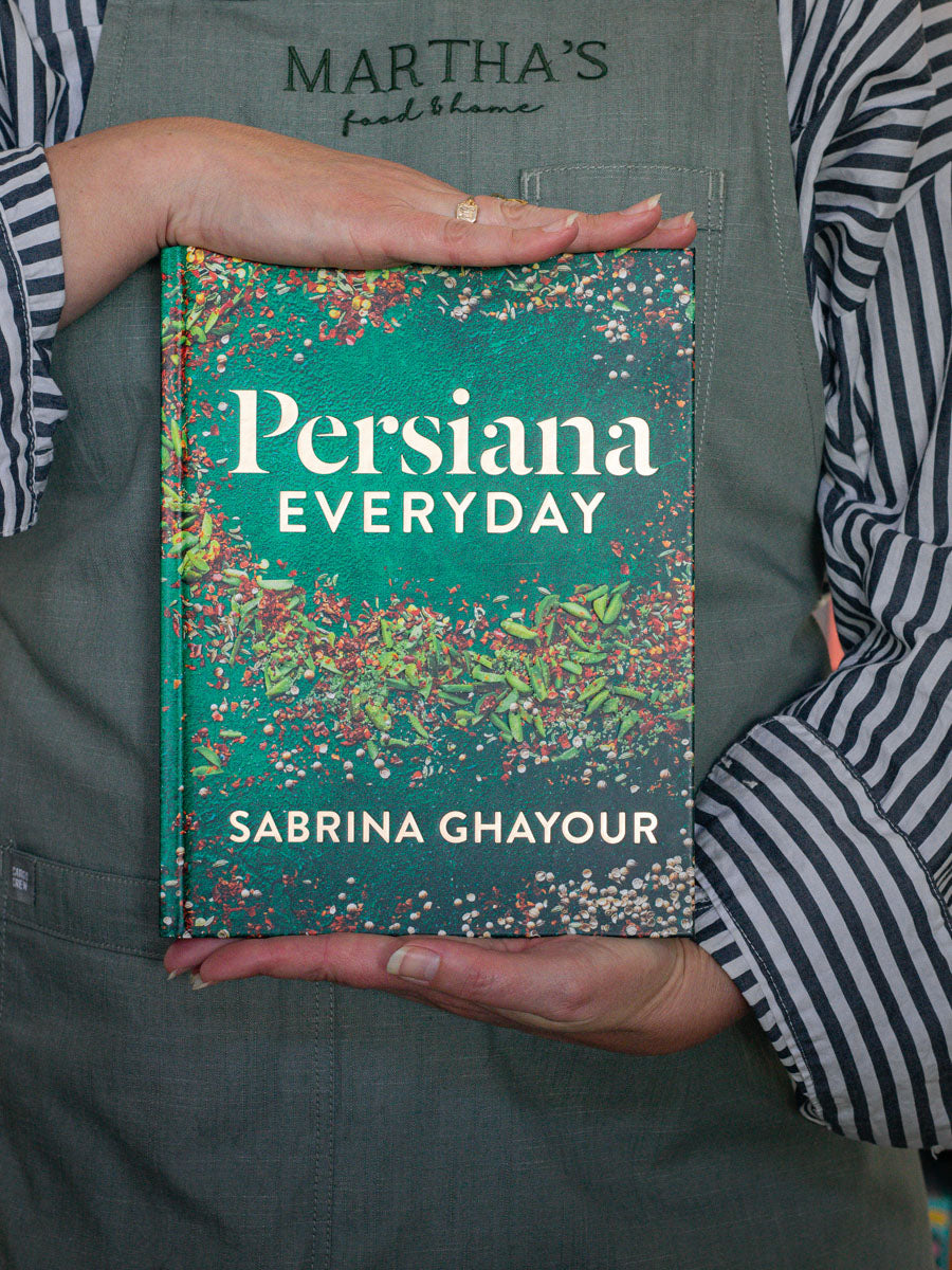 A person holding a book titled 'Persiana Everyday' by Sabrina Ghaour, featuring a green and multicolor floral design on the cover.