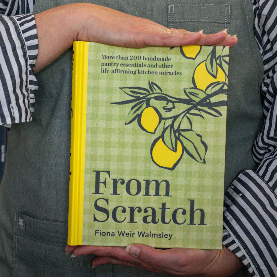 A person holding a book titled 'From Scratch' by Fiona Wealsley, featuring a lemon tree on the cover.