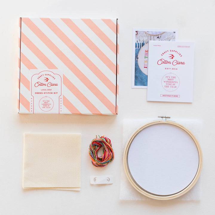 Embroidery kit with cross-stitch hoop, fabric, materials, and pattern on a white background