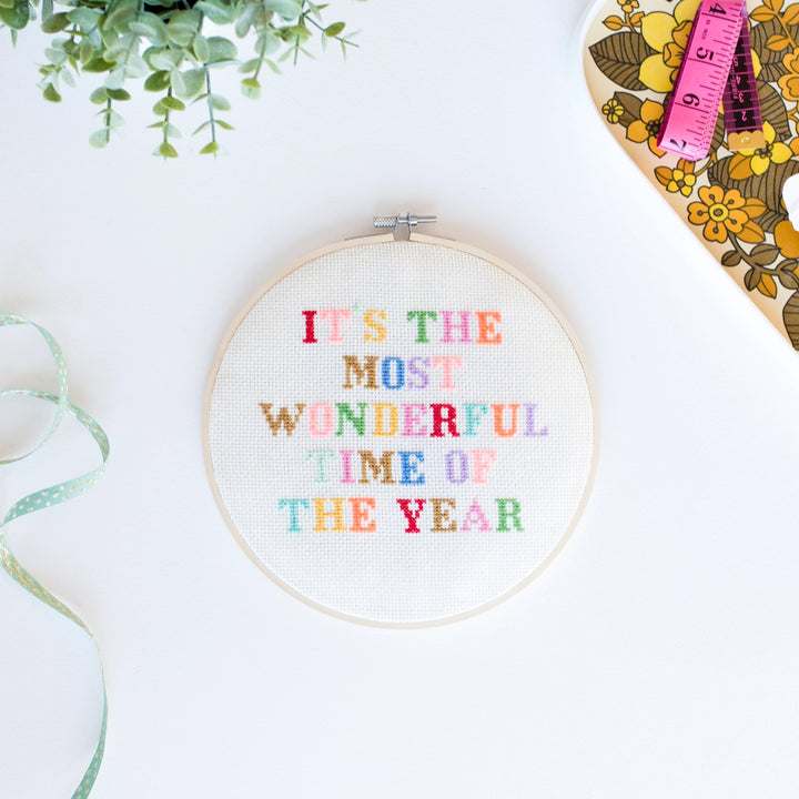 Embroidery hoop with colorful text 'It's the most wonderful time of the year' on a white background.