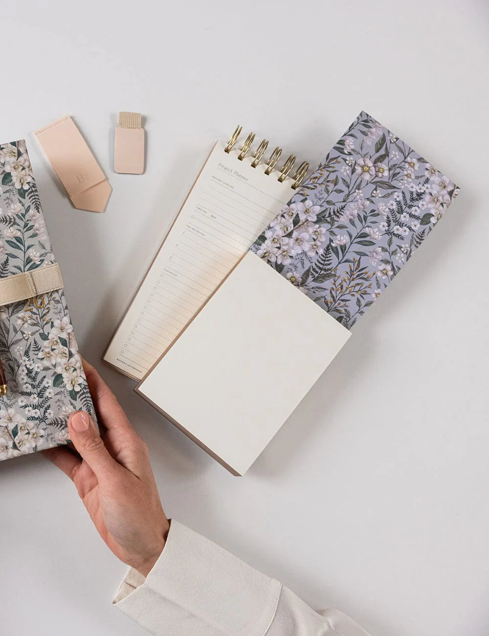 Hand holding a floral notebook with other notebooks and stationery on a light surface