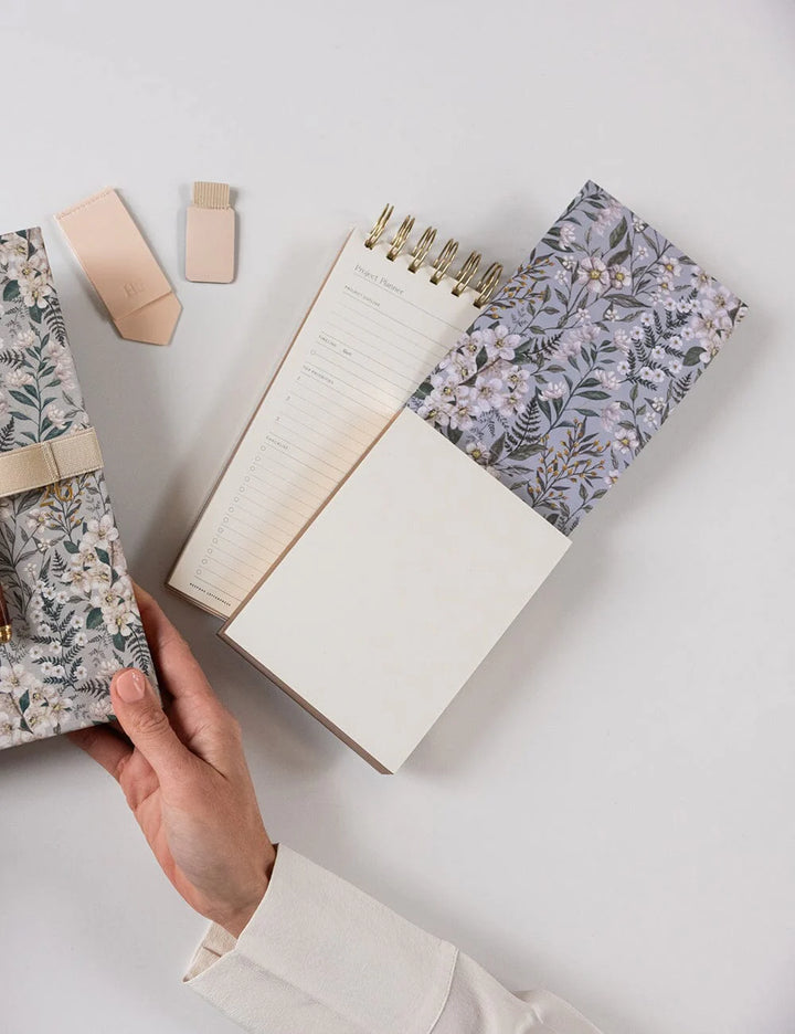 Hand holding a floral notebook with other notebooks and stationery on a light surface