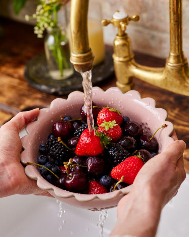 Person washing berries in a pink berry bowl under running water from a faucet.