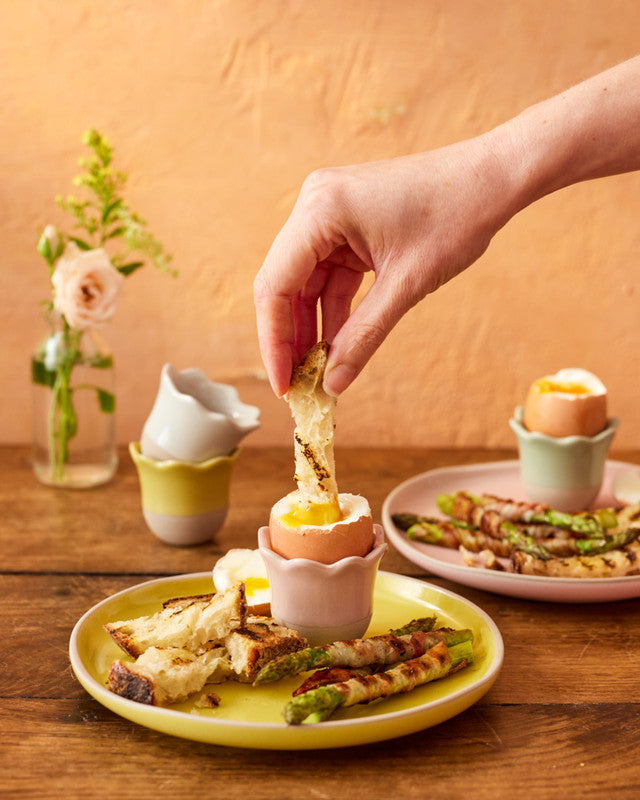 Person dipping bread into a soft-boiled egg on a wooden table with a blurred background