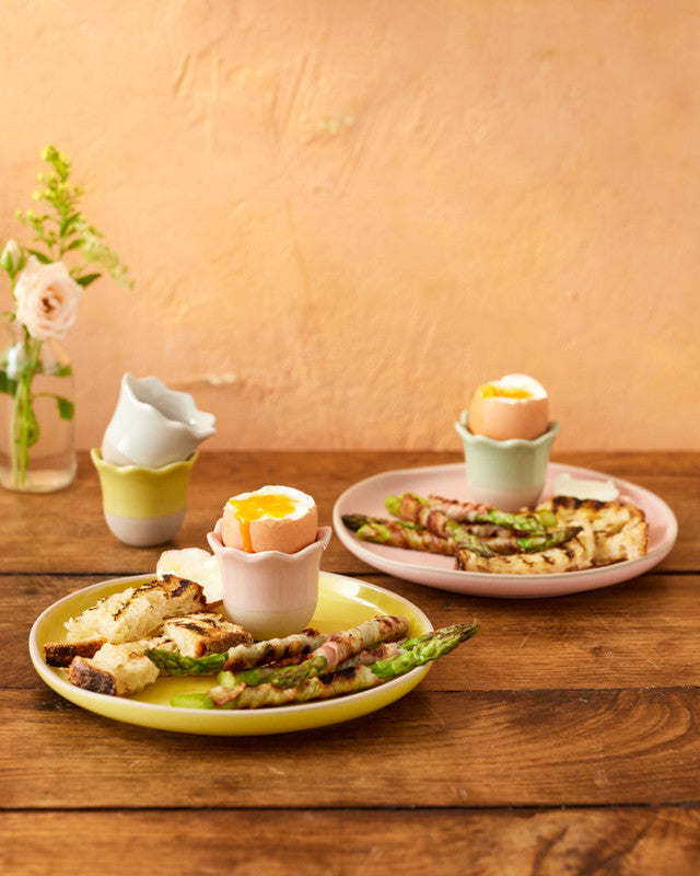 Plates of food with boiled eggs in egg cups on a wooden table with a warm background