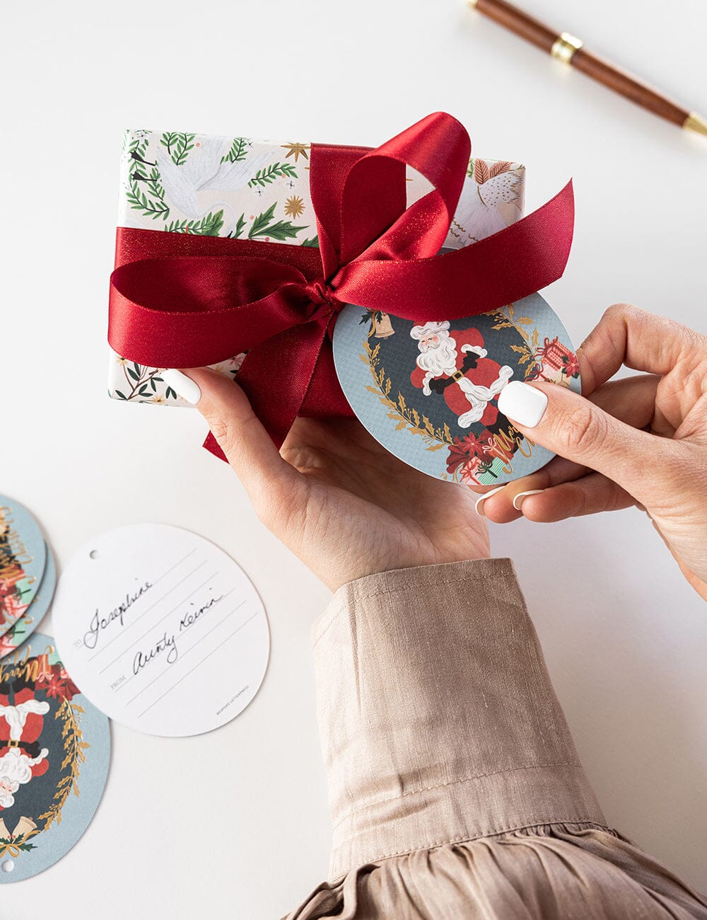 Hand holding a gift wrapped in red ribbon with Christmas-themed coasters on a light background