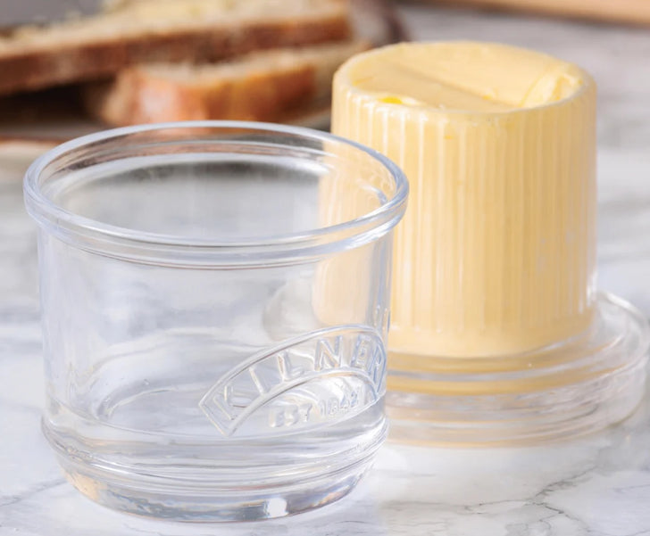 Butter container with a stick of butter next to a glass on a marble surface