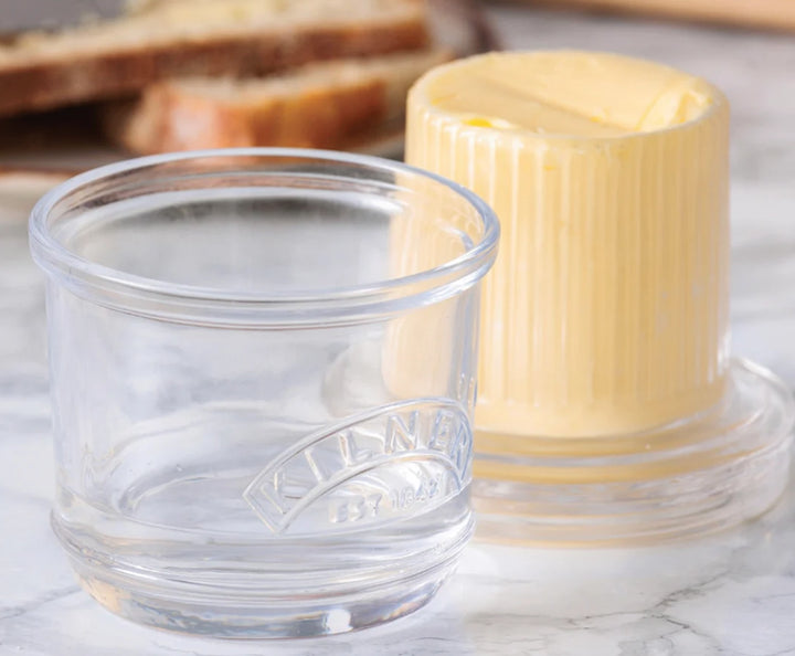 Butter container with a stick of butter next to a glass on a marble surface