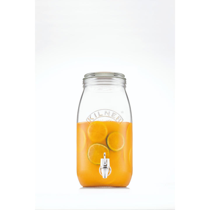 Clear glass drink dispenser filled with orange juice on a white background