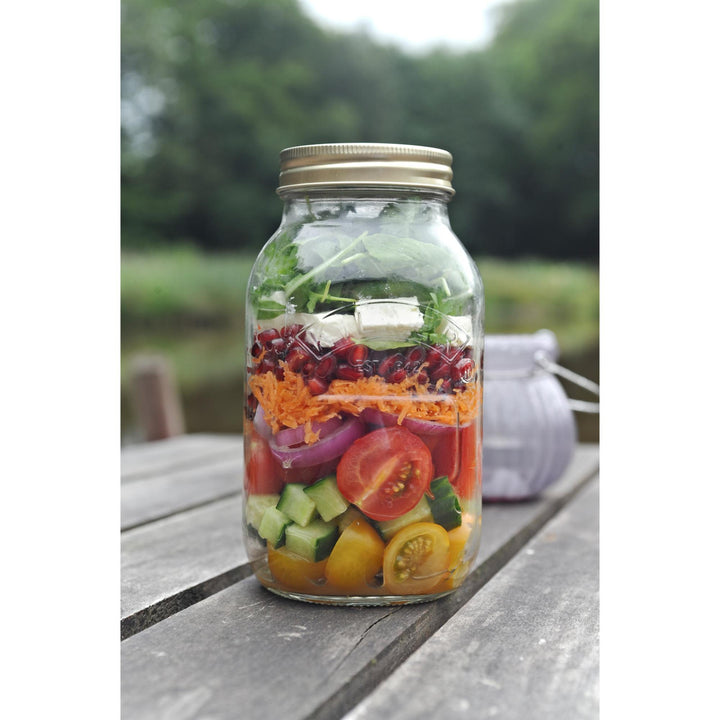 Glass jar with layered salad on a wooden surface outdoors