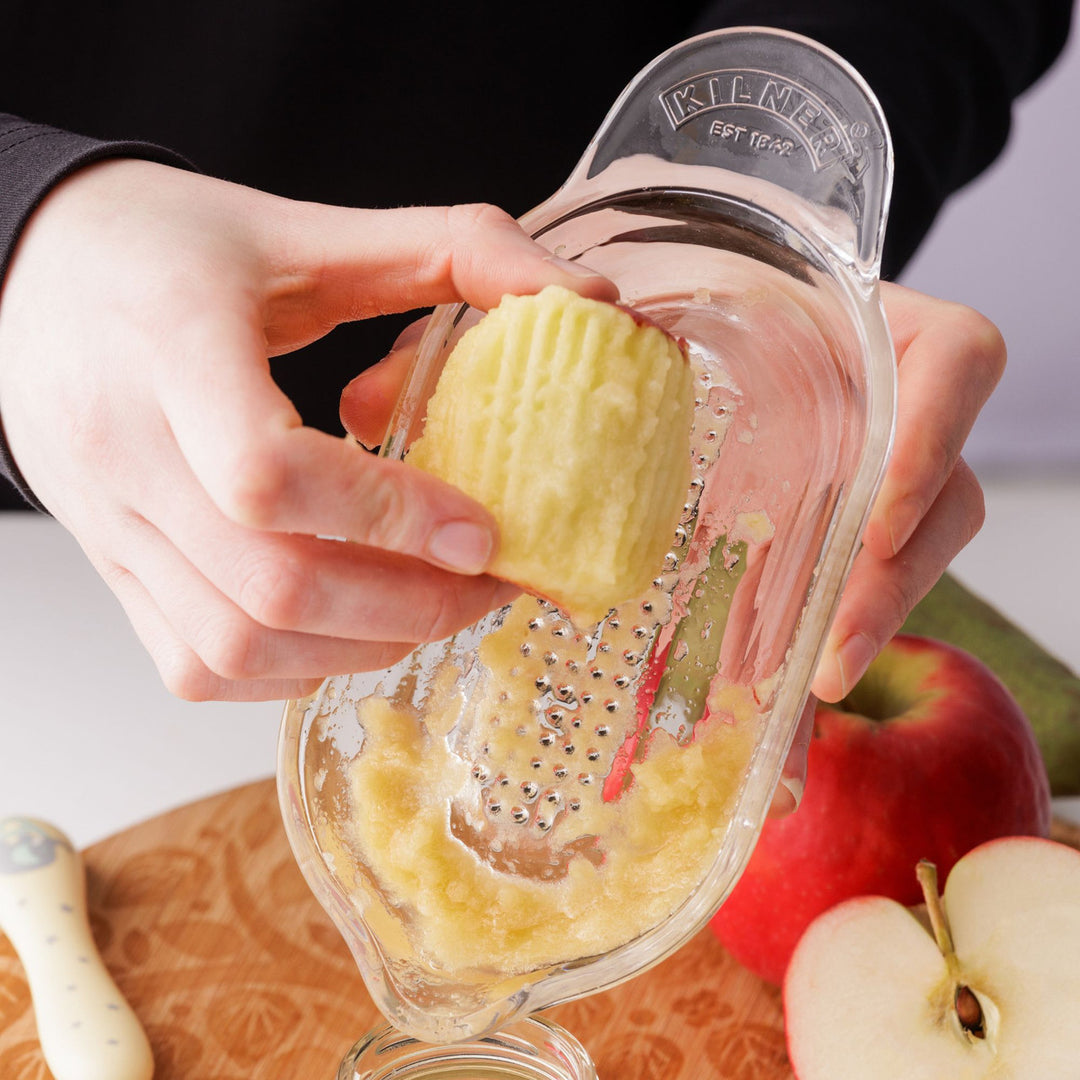 Person using a grater to peel an apple with apples in the background
