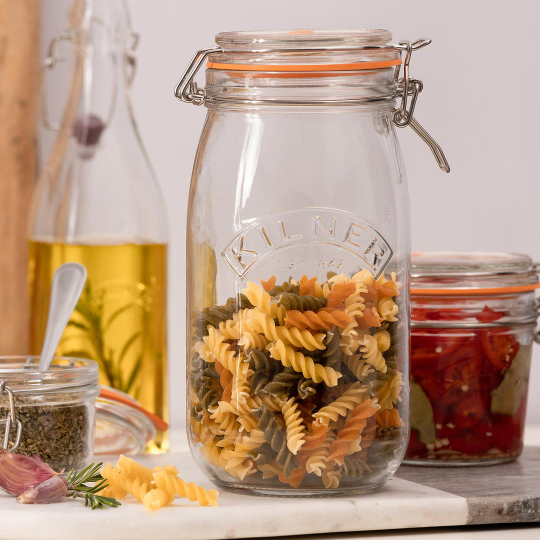 Glass jar filled with multicolored pasta on a kitchen counter with other jars and ingredients.