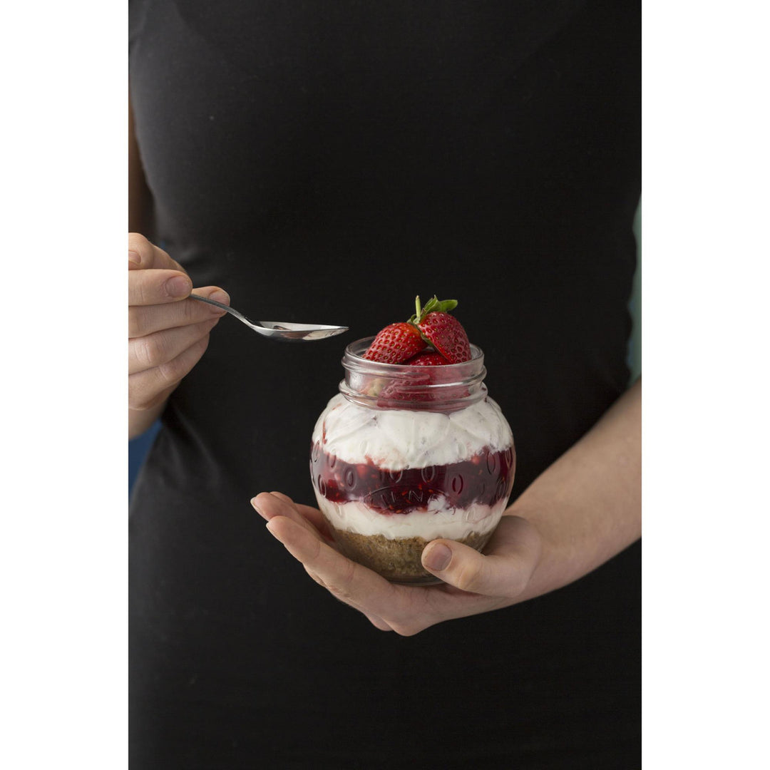 Person holding a jar of dessert with strawberries and a spoon
