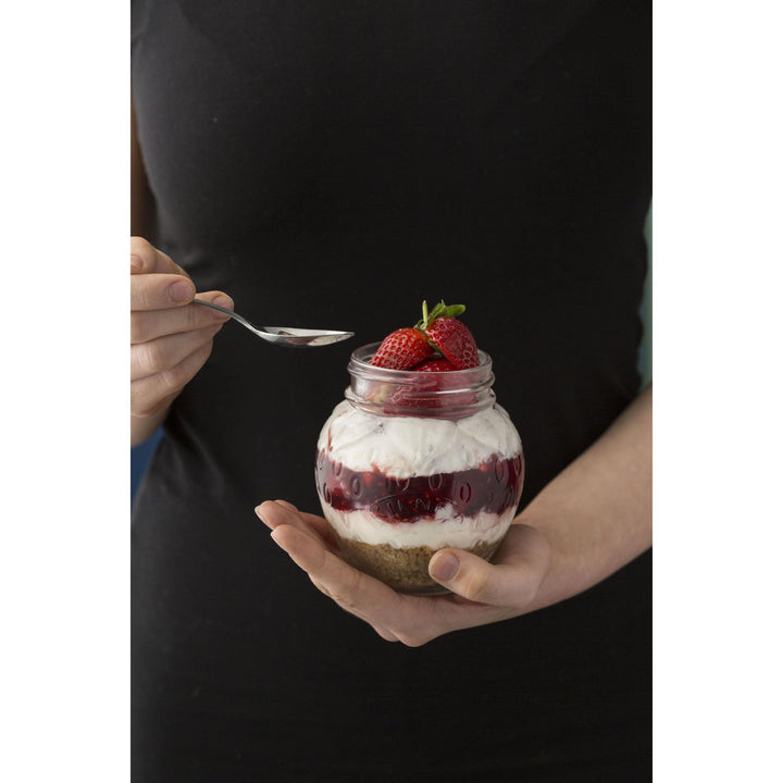 Person holding a jar of dessert with strawberries and a spoon