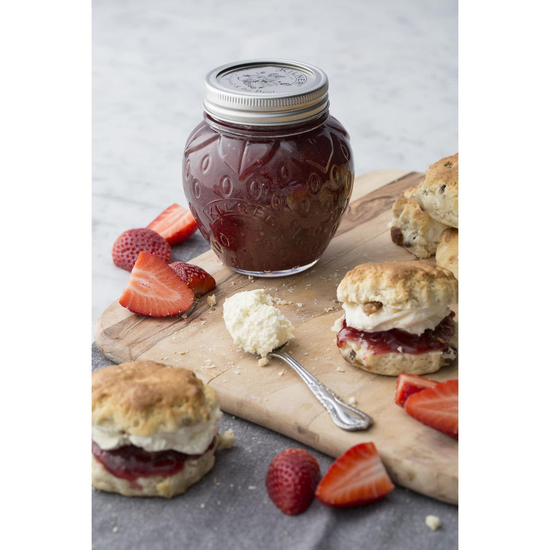 Jar of jam on a wooden board with scones and strawberries