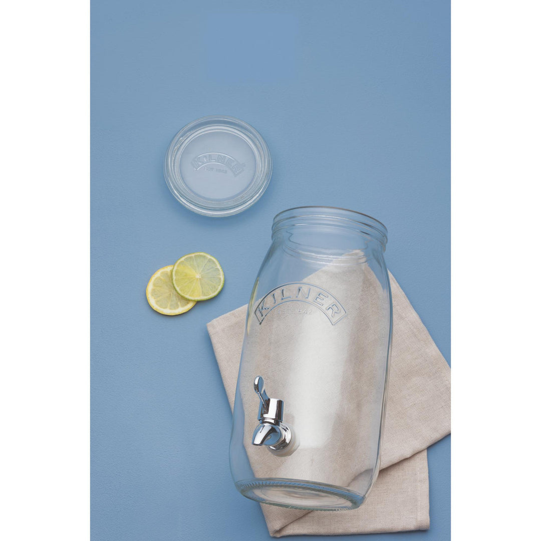Clear glass drink dispenser with a silver faucet on a blue background