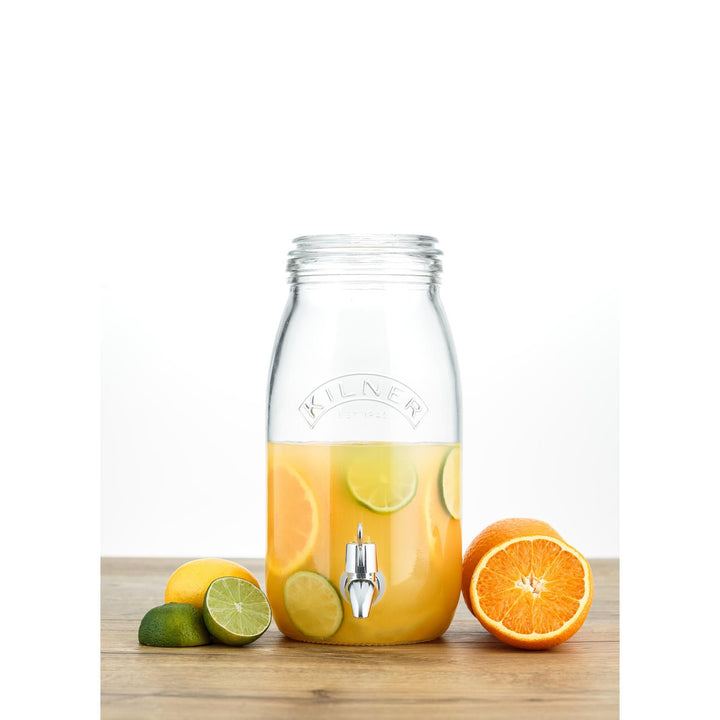 Clear glass drink dispenser with lemon and orange slices on a wooden surface