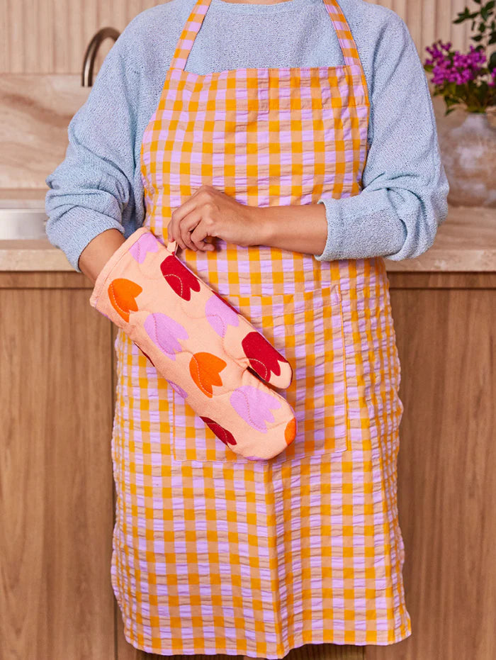 Person wearing a yellow checkered apron holding a colorful hot dog-shaped object.