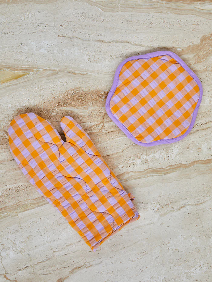 Orange and white checkered oven mitt and pot holder on a beige marble surface