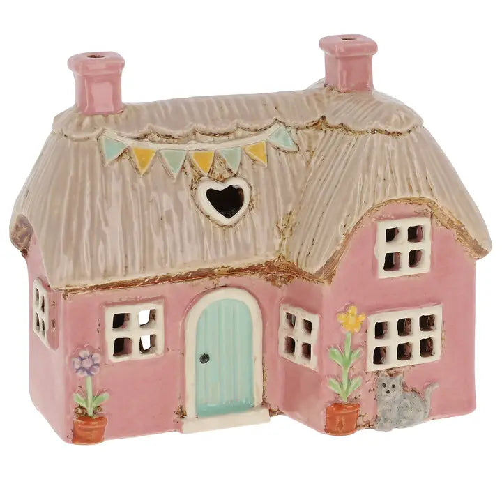 Small pink cottage tealight holder with a thatched roof and decorative elements on a white background