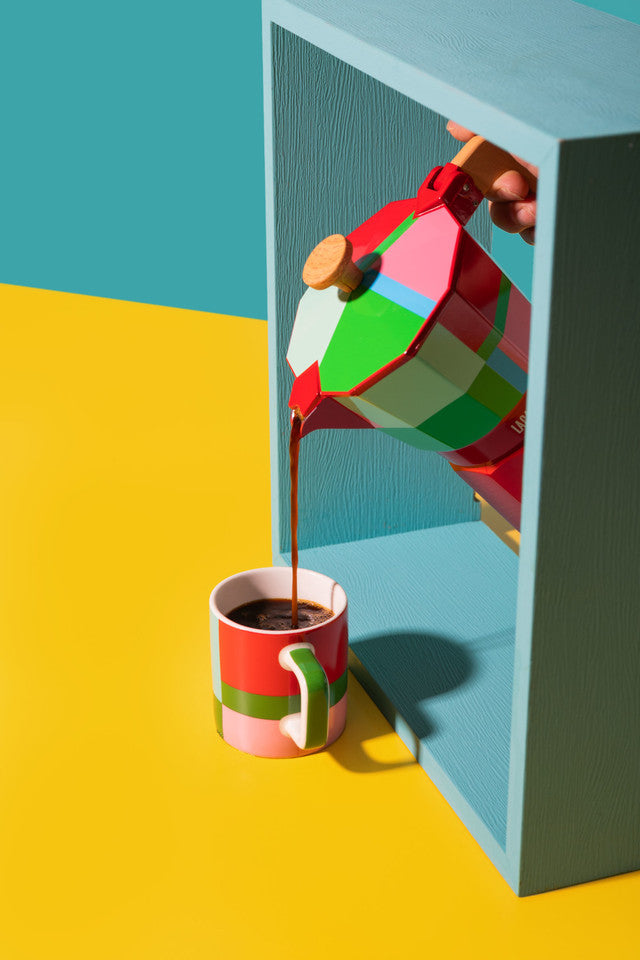 Colorful coffee maker pouring coffee into a mug on a blue and yellow background