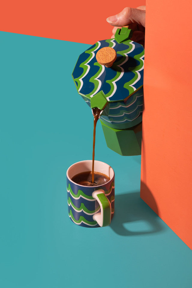 Colorful coffee pot pouring coffee into a matching cup against a vibrant background