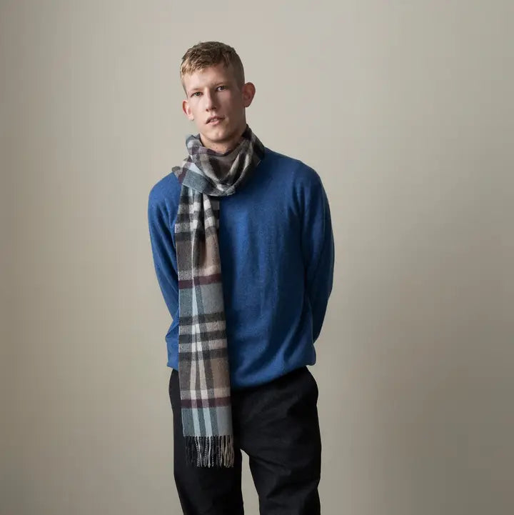 Man wearing a blue sweater and plaid scarf against a plain background