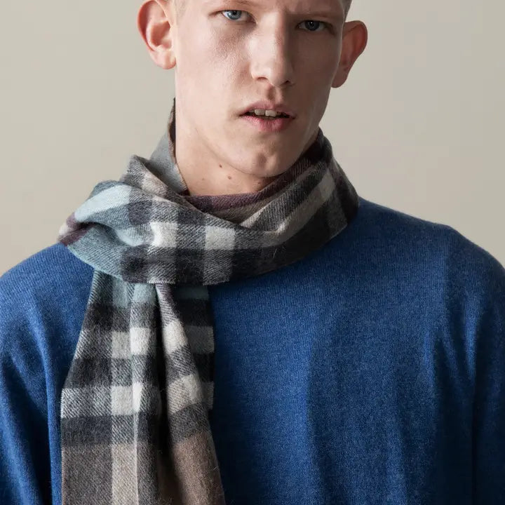 Man wearing a blue sweater and plaid scarf against a neutral background