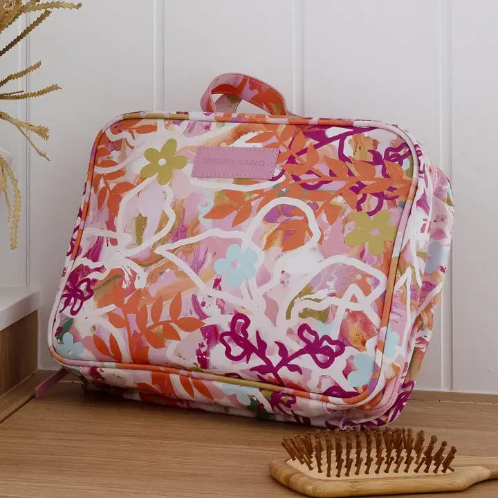 A floral toiletry bag with a pink, orange, and white pattern, resting on a wooden surface against a white paneled wall.