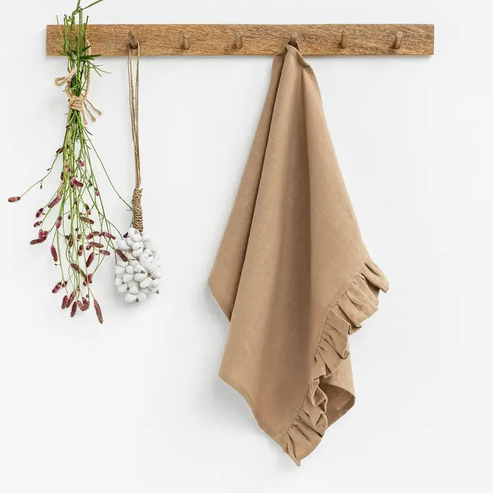 Beige towel hanging on a wooden rack with decorative plants against a white background