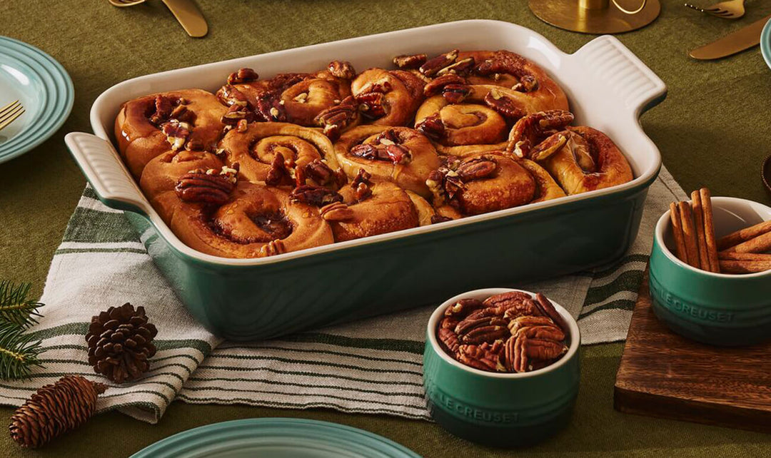 Baked cinnamon rolls with pecans in a teal dish on a green tablecloth.