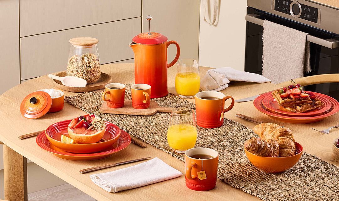 Breakfast setup on a wooden table with  orange ceramic dishes and glasses.