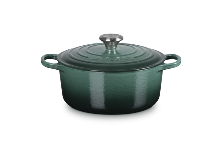 Green enameled cast iron Dutch oven with a lid on a white background