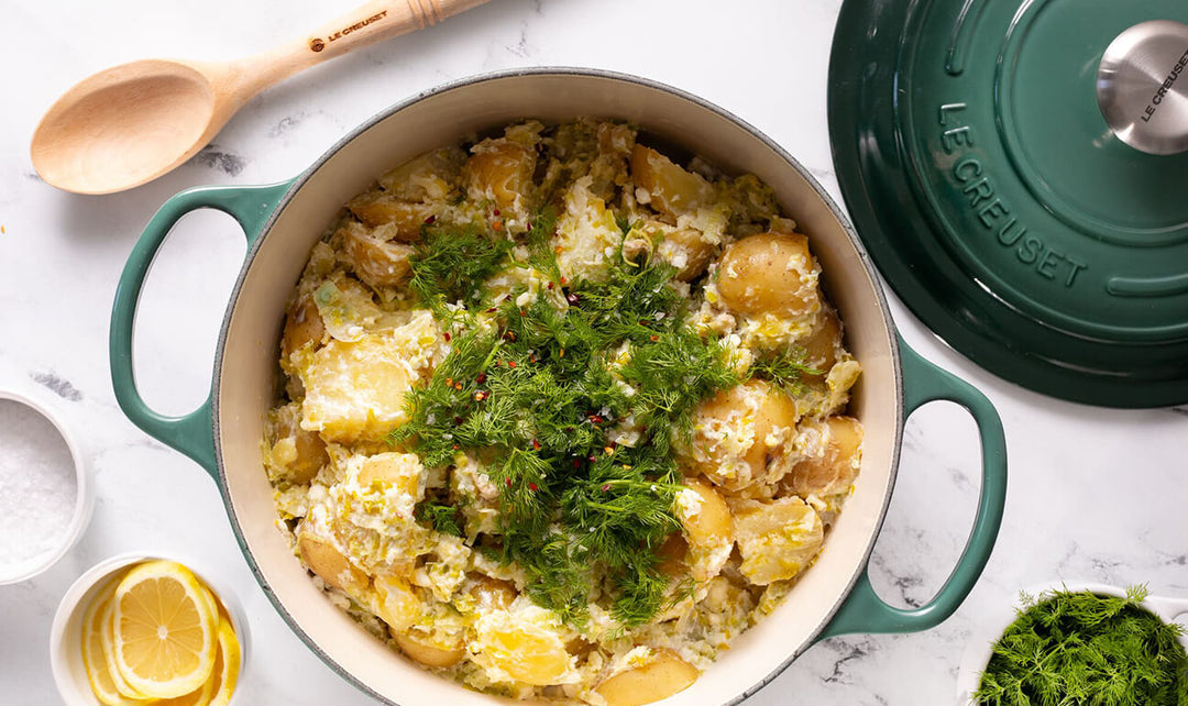 Dish of creamy potatoes with herbs in a Le Creuset pot on a marble surface.