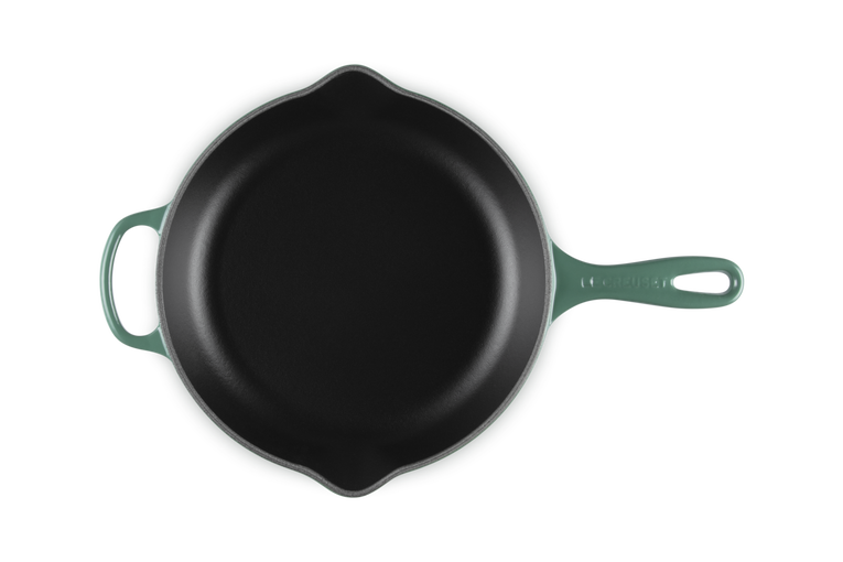 Black cast iron skillet with green handle on a white background