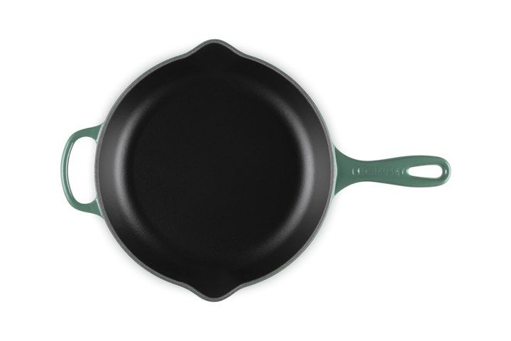 Black cast iron skillet with green handle on a white background
