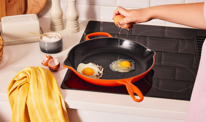 Person cooking eggs in a red skillet on a stove