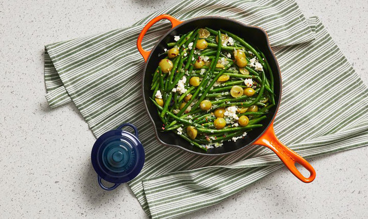 Skillet with green beans and cherry tomatoes on a striped towel