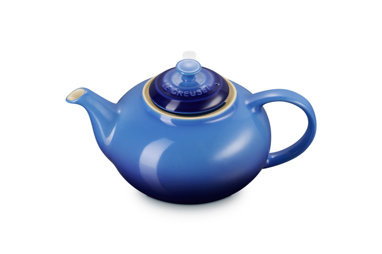 Blue Le Creuset teapot with a lid on a white background